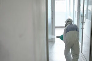 Disinfecting of office to prevent COVID-19, person in white hazmat suit with disinfect in office, coronavirus concept